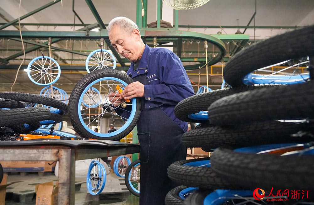 在浙江省慈溪市觀海衛鎮一童車企業，工人在生產線上安裝輪回光。人民網 章勇濤攝