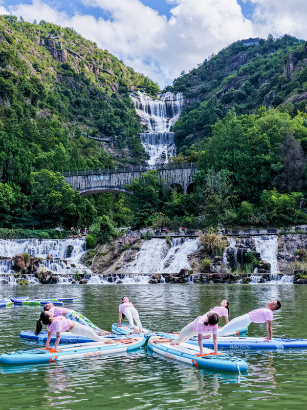 天臺山大瀑布前，槳板瑜伽選手分列水面，身體后仰如滿弓，與飛瀑構成力與美的對話。浙江省體育局供圖